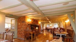 L’intérieur d’un restaurant présente des planchers en bois, des murs en briques et une cheminée en briques. Des tables et des chaises sont disposées pour accueillir les clients.