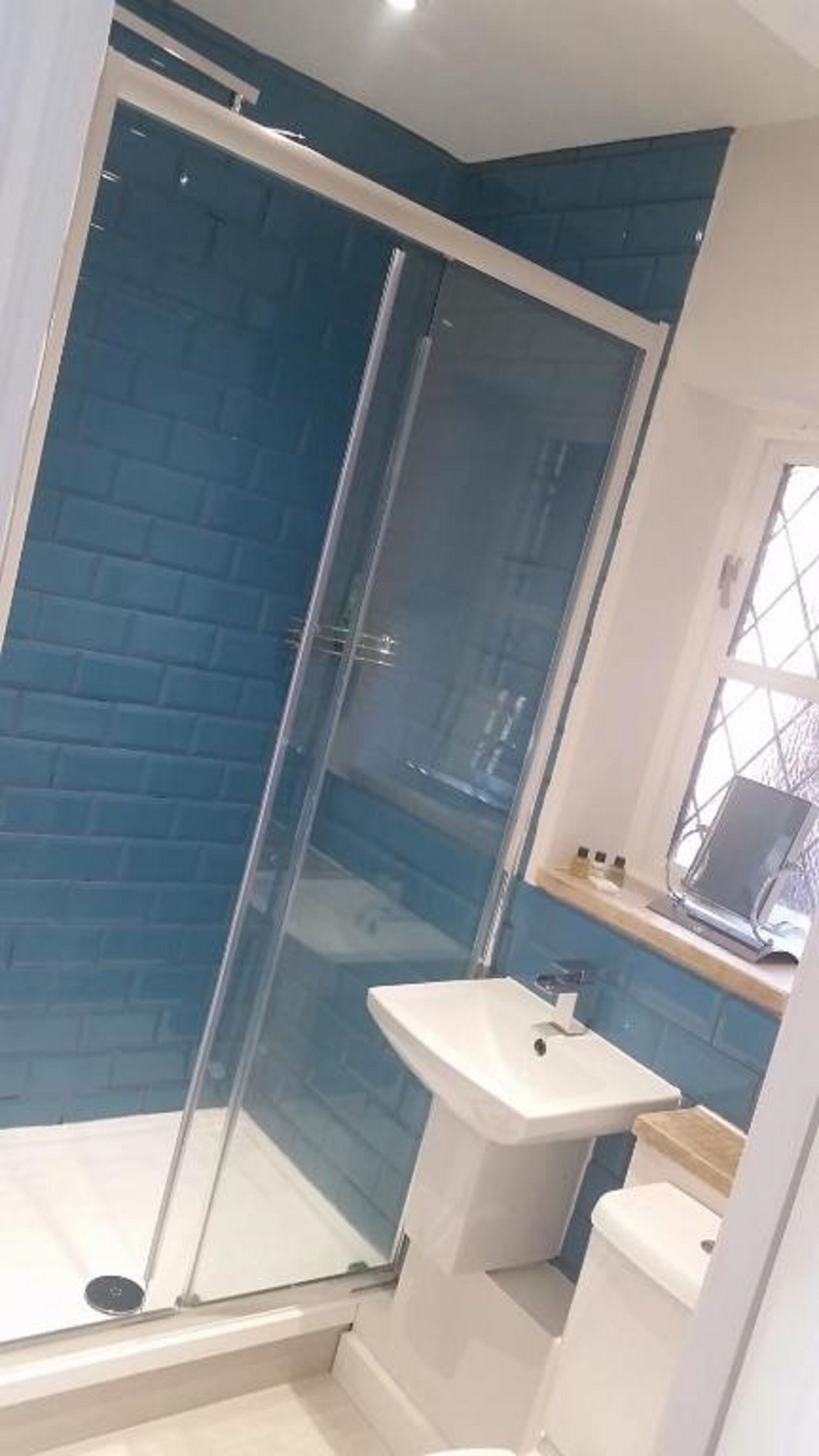 A bathroom with a glass shower enclosure, a white sink, and a window.