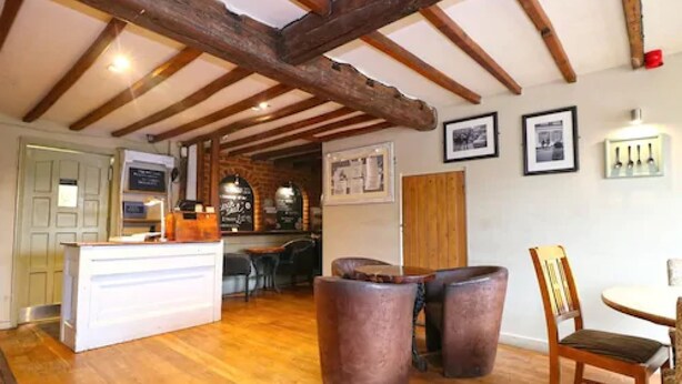 Un intérieur rustique avec des poutres apparentes, un bar en bois et un espace détente composé d’une table et de chaises.