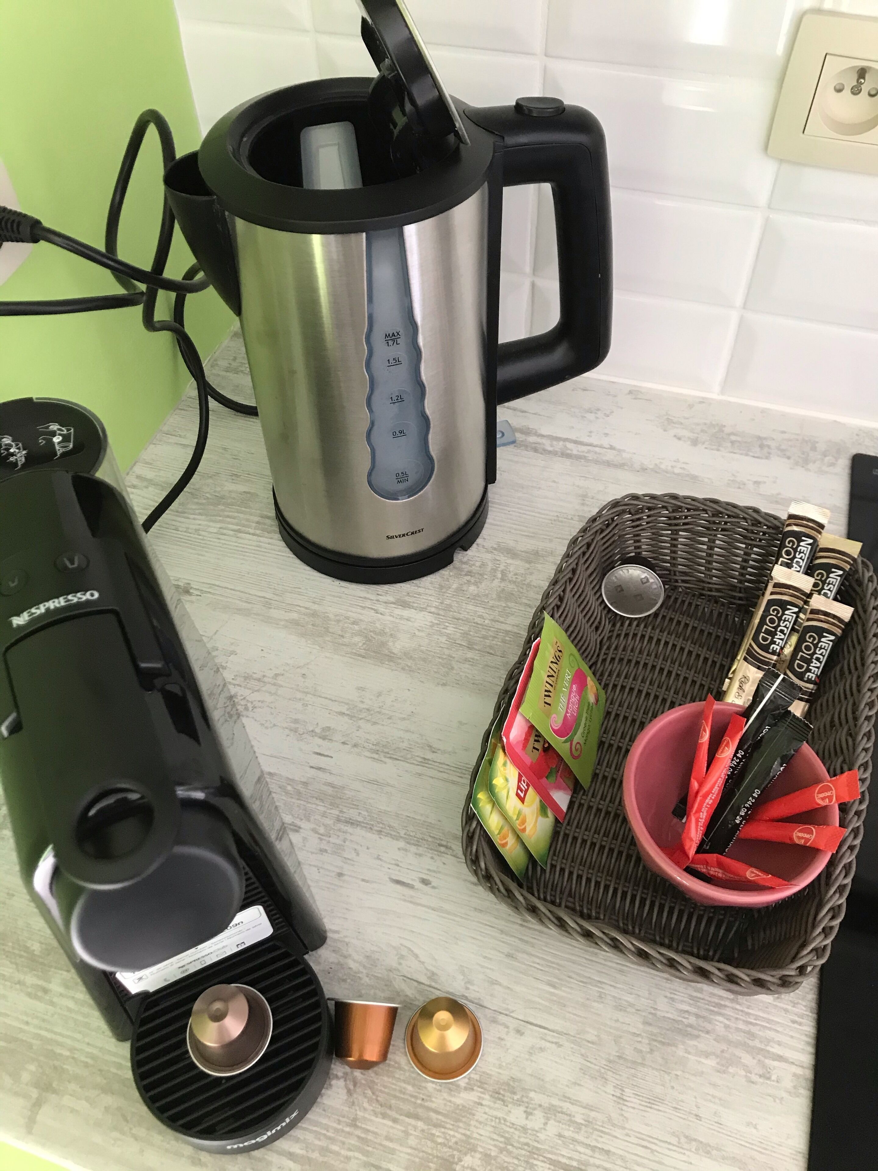 Una cocina con cafetera, hervidor y una cesta con cápsulas de café.