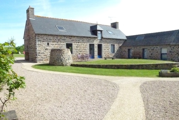A stone building with a sloped roof, a gravel driveway, and a small lawn area.
