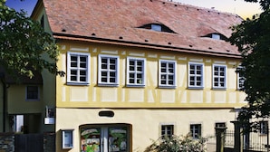 Ein gelbes Gebäude mit rotem Ziegeldach, mehreren Fenstern und einem kleinen Eingang mit einem Schild.