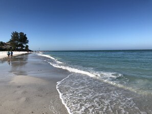A beach with clear water, a sandy shore, and a few people walking.