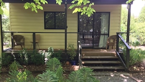 A covered porch with two wicker chairs, a small table, and a staircase leading to a door. - Stand alone cottage in tranquil garden, with balcony, pergola, SkyTV, free Wifi (Greytown)