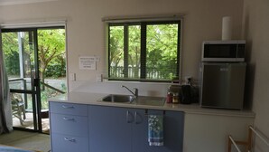 A compact kitchen with a sink, a microwave, and a refrigerator. There is a window with blinds, and a sign on the wall. - Stand alone cottage in tranquil garden, with balcony, pergola, SkyTV, free Wifi (Greytown)