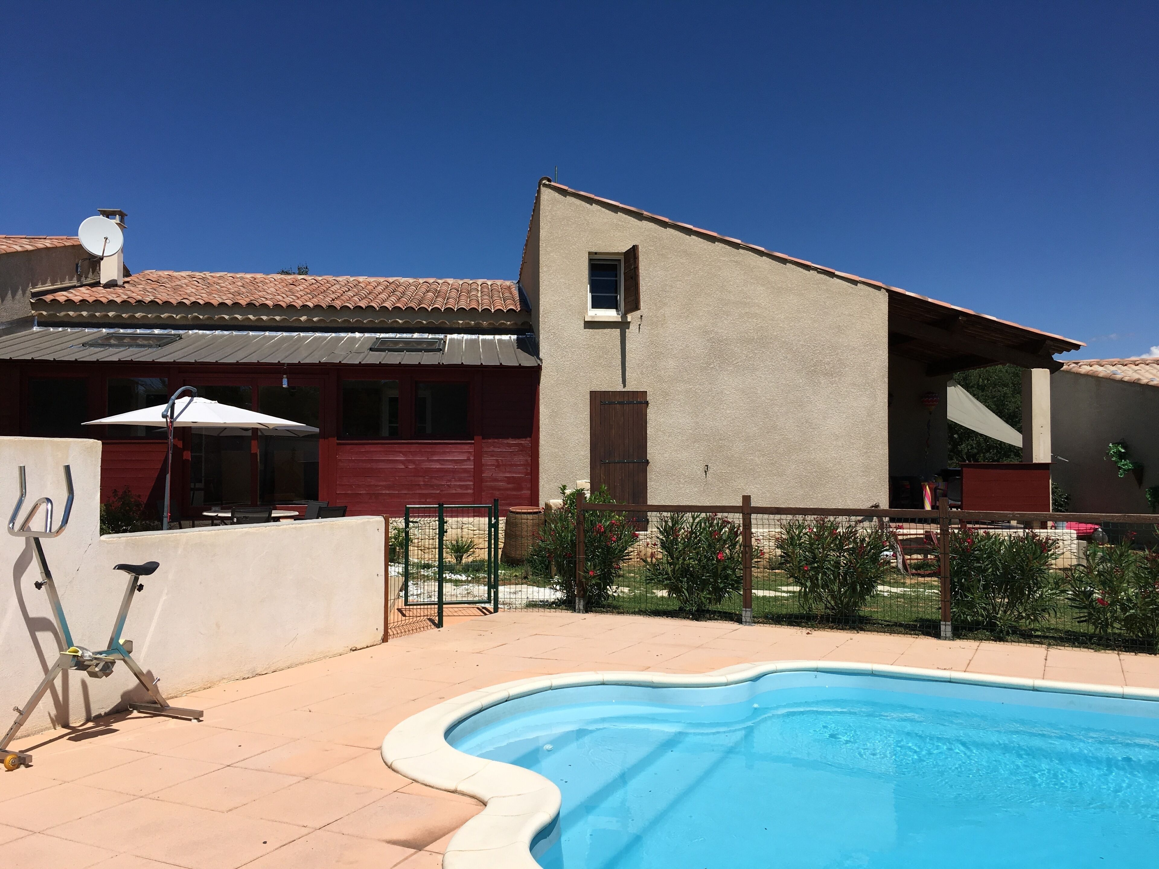 A house with a swimming pool, a patio with a table and chairs, and a fenced garden area.