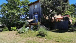 Een houten huis met twee verdiepingen en een balkon, omringd door een houten hek en diverse planten.