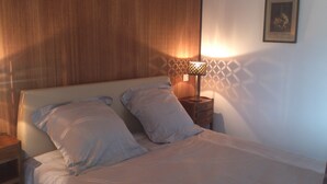 Een net opgemaakt bed met kussens, een nachtkastje, een lamp en een muur met een geometrisch patroon.