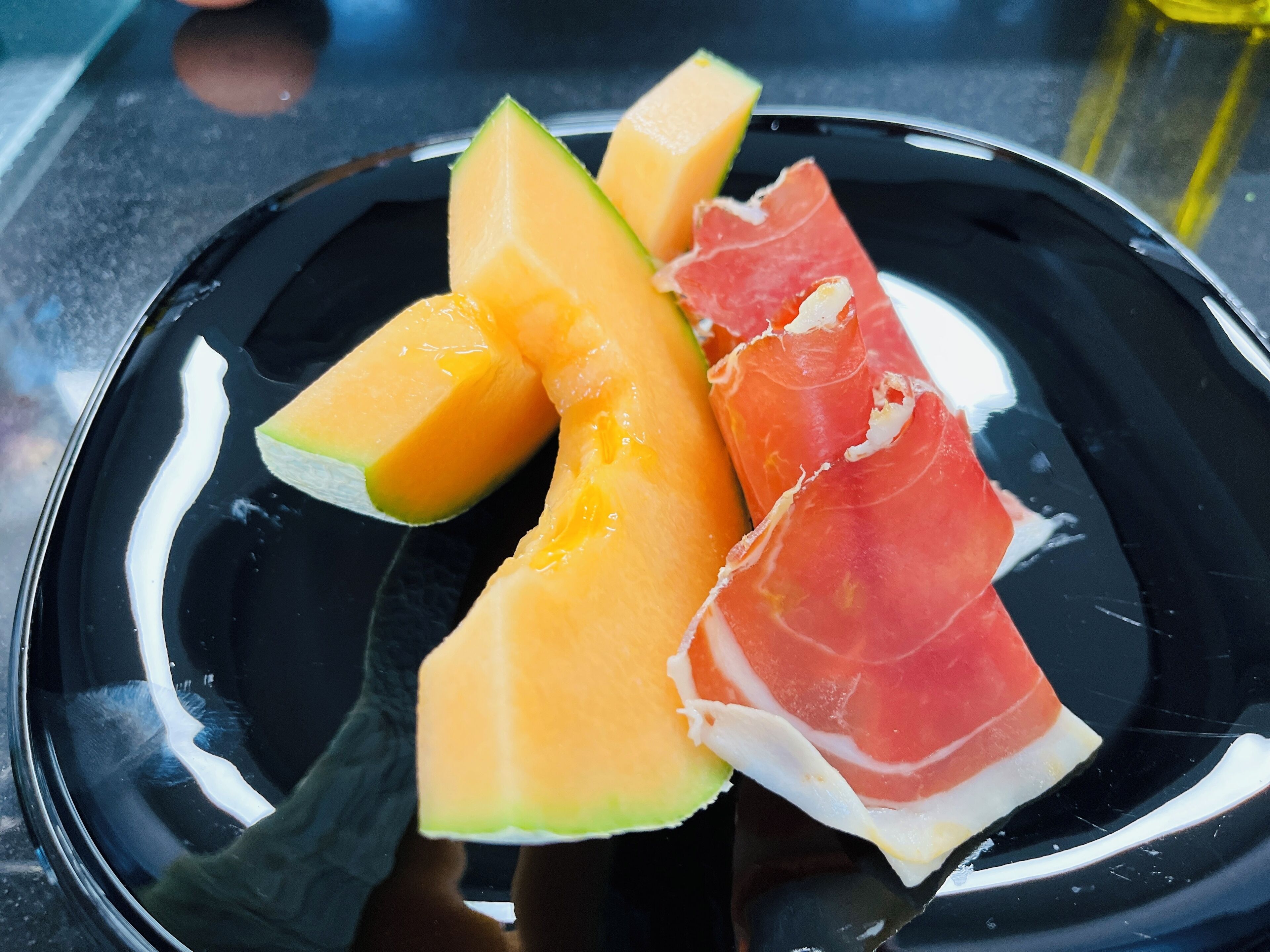Une assiette noire garnie de melon cantaloup et de jambon de Parme.