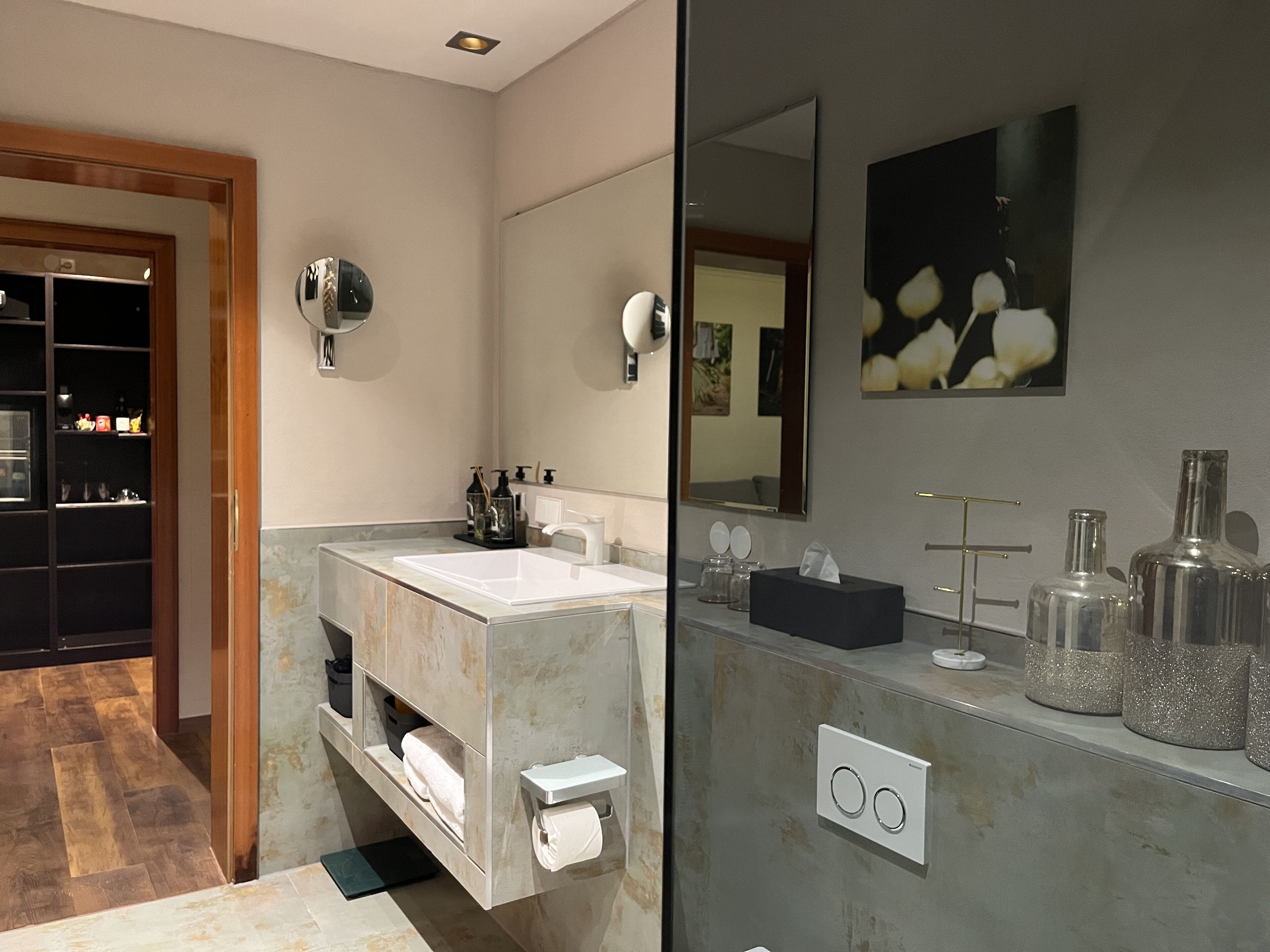 A modern bathroom with a marble sink, a large mirror, and a shelf with toiletries.