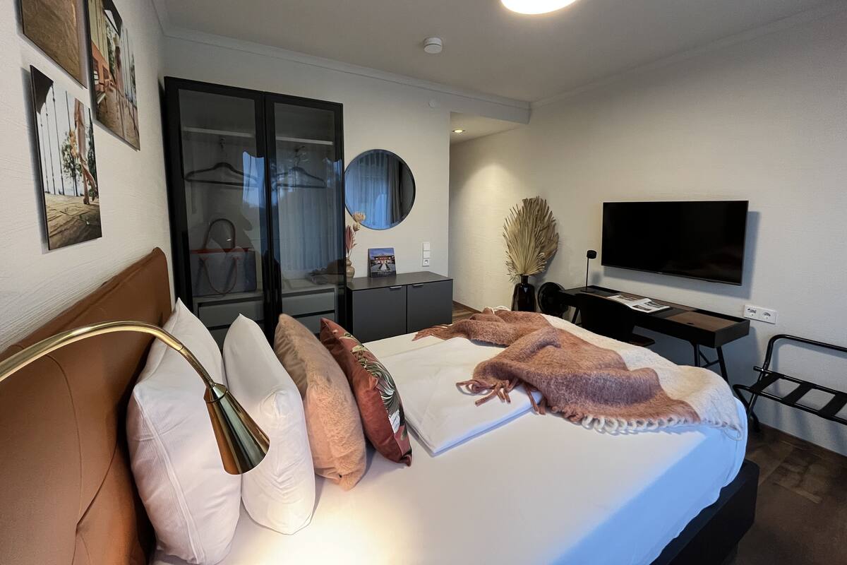 A modern hotel room with a bed, a desk, a TV, and a wardrobe.