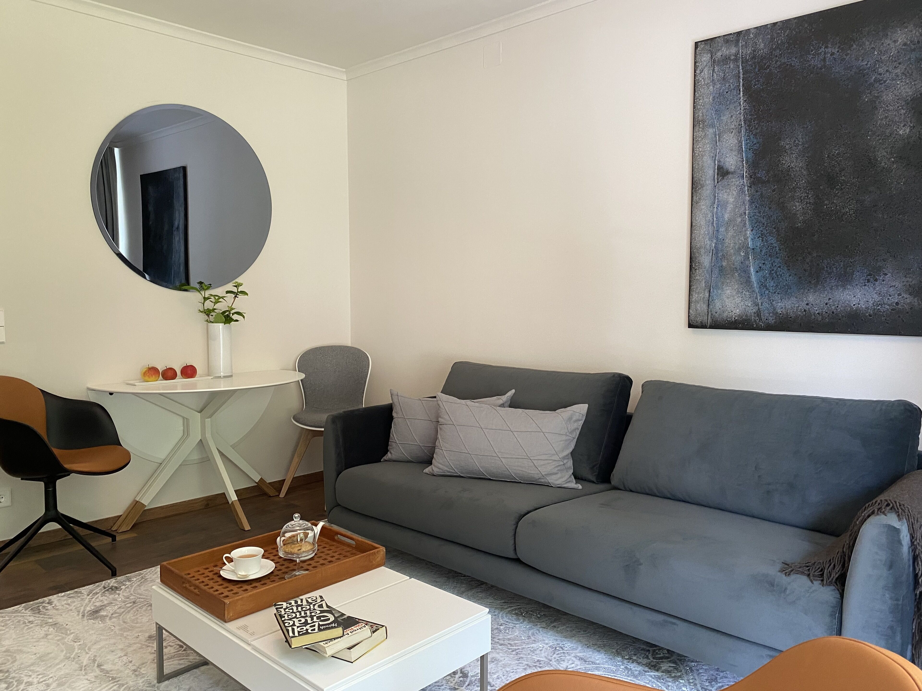 A modern living room with a grey sofa, a round mirror, a small white table, and a coffee table with a tray and book.