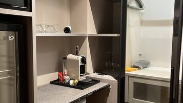 Una kitchenette compacta con cafetera, un lavamanos pequeño y un armario de vidrio.