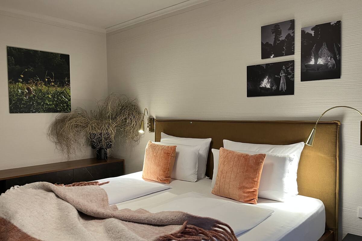 A hotel room with a large bed, a nightstand, a lamp, and wall art.
