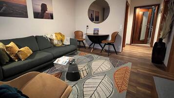 A living room with a sofa, a coffee table, a round mirror, and a dining area with chairs.