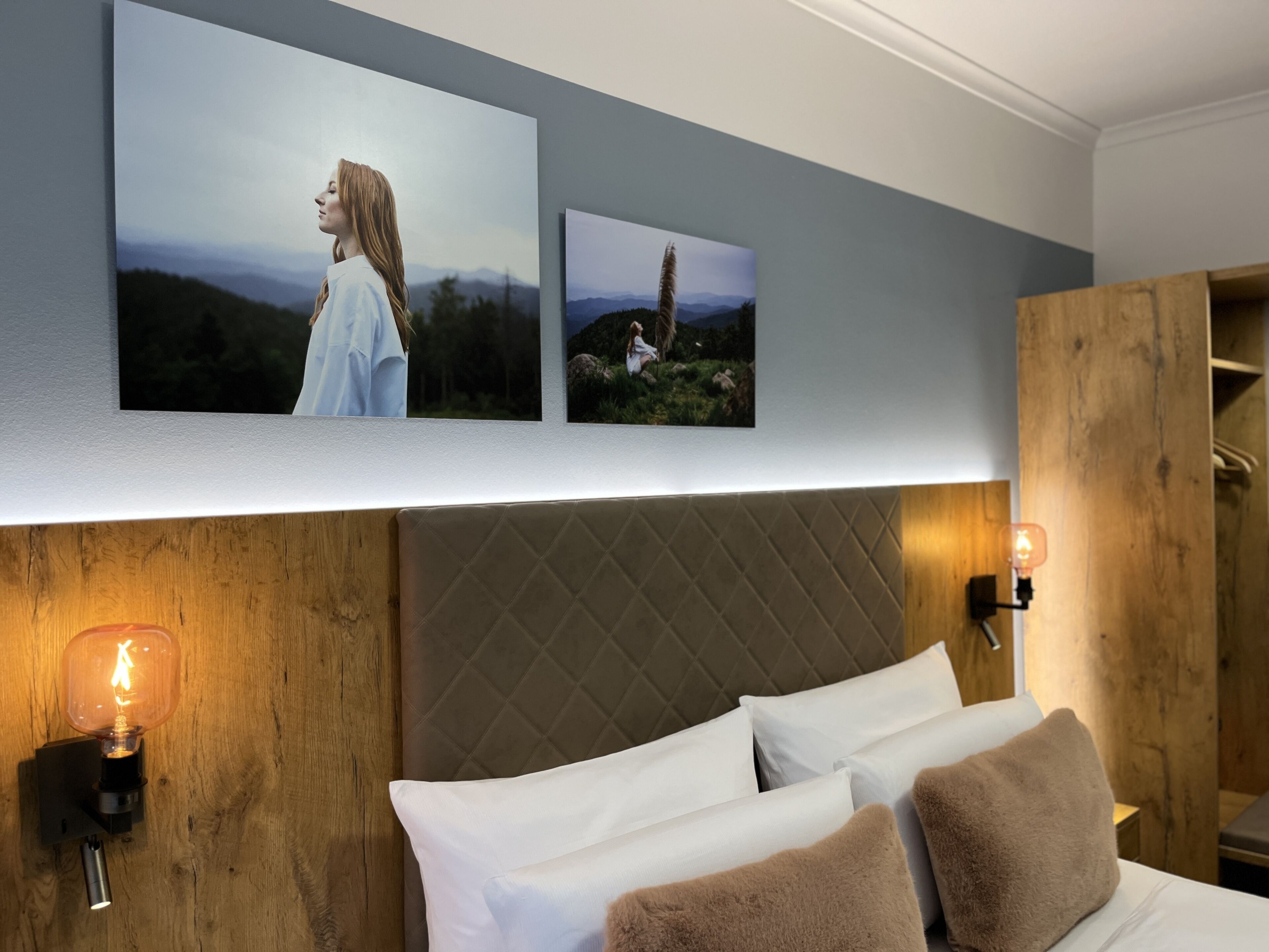 Une chambre d’hôtel avec un lit, une tête de lit en bois et des cadres photo accrochés au mur.