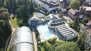 An aerial view of a hotel complex with a large glass building, a swimming pool, and surrounding greenery. - Hotel Schlossberg (Badenweiler)