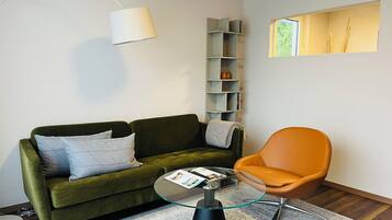 A modern living room with a green sofa, an orange chair, a glass coffee table, and a white lamp.