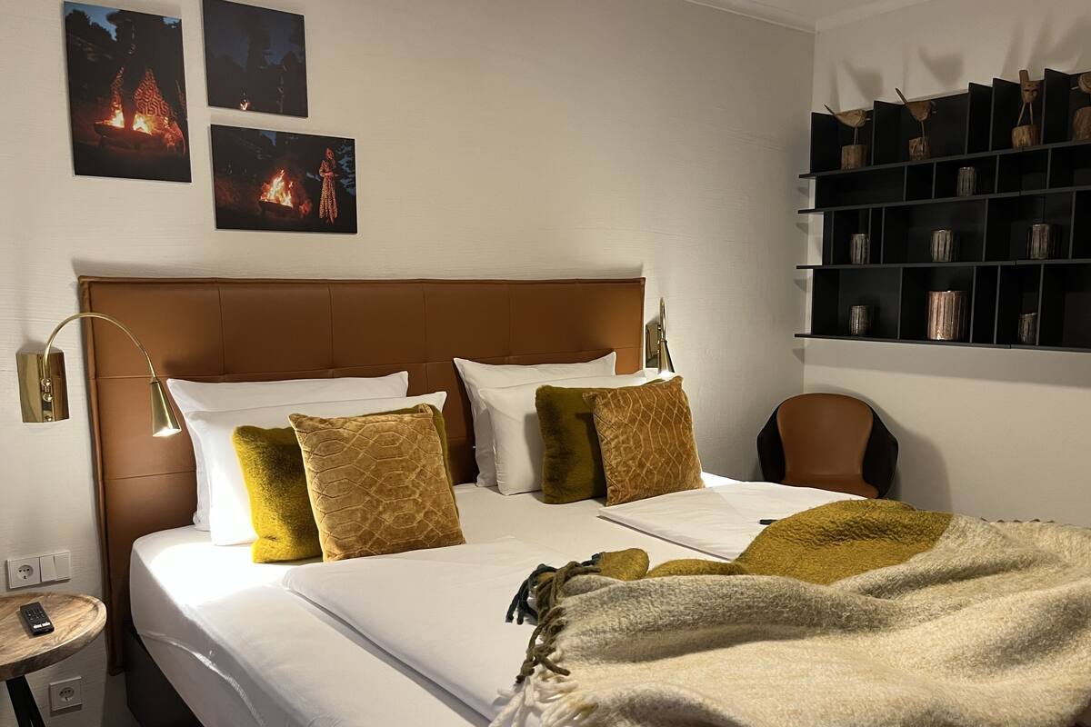 A hotel room with a large bed, a nightstand, a lamp, and a shelf with decorative items.