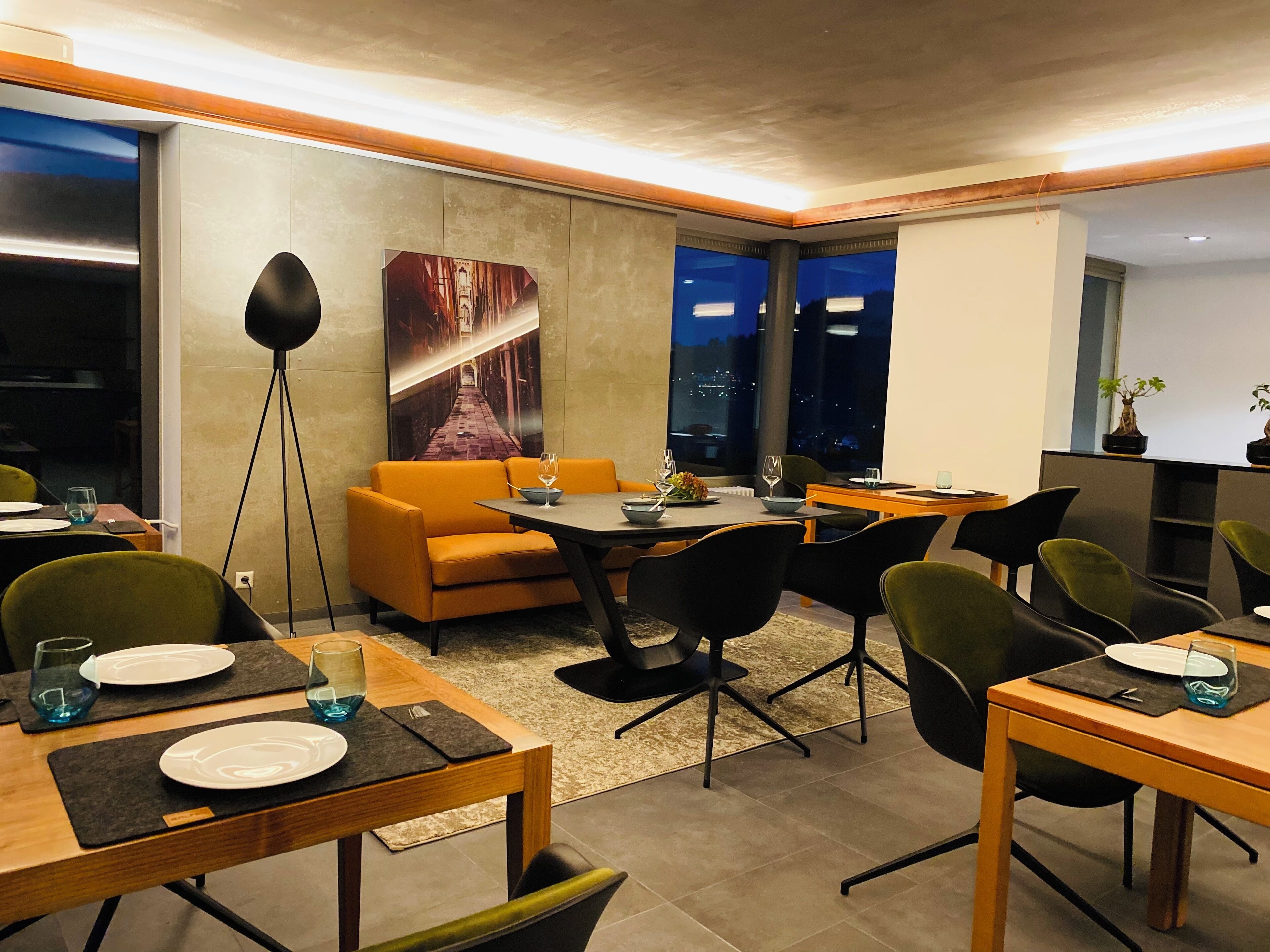 Un espace repas moderne avec une table en bois, des chaises noires et un canapé orange vif.