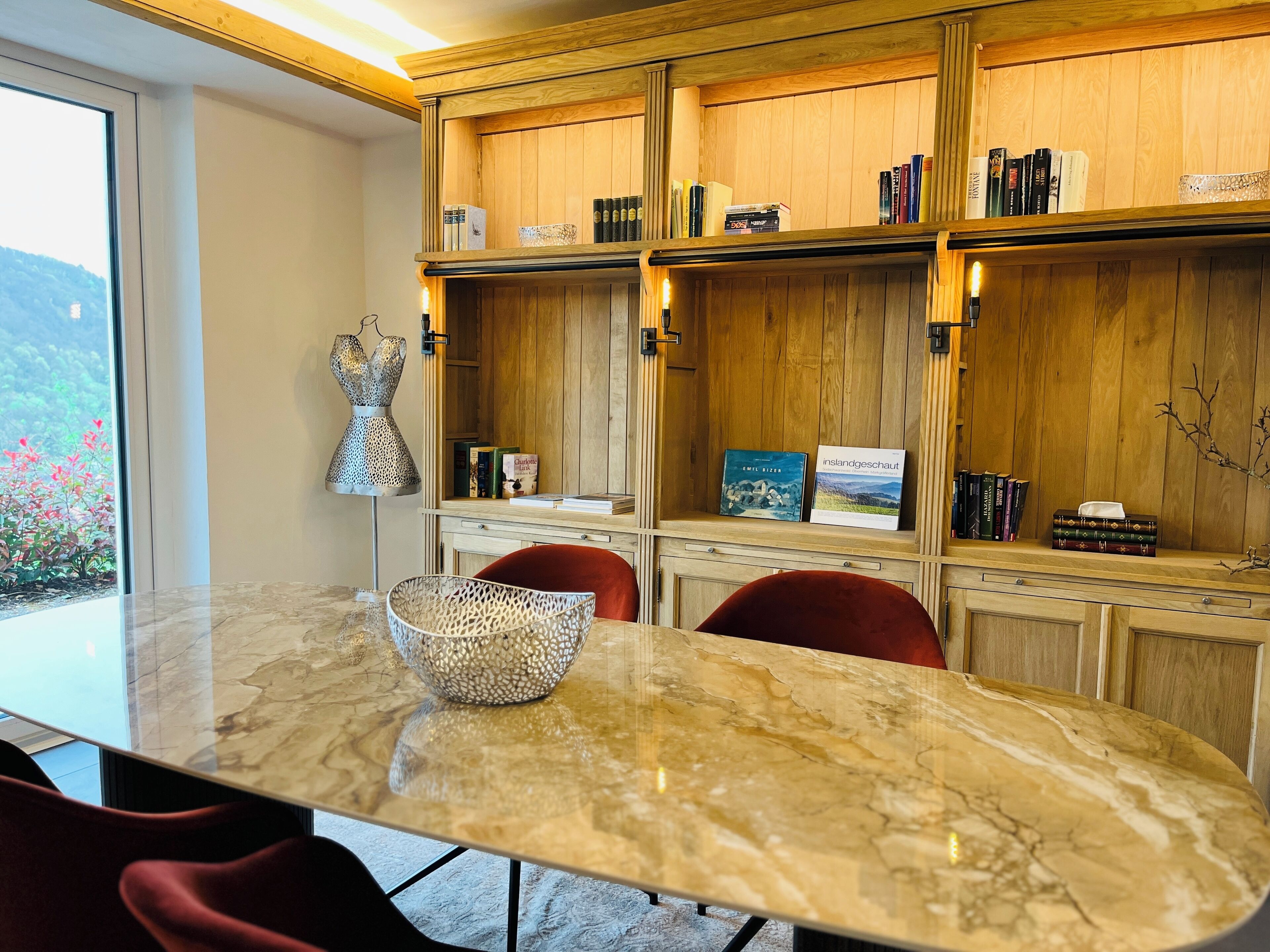 A modern dining area with a marble table, red chairs, and wooden bookshelves filled with books and decorative items.