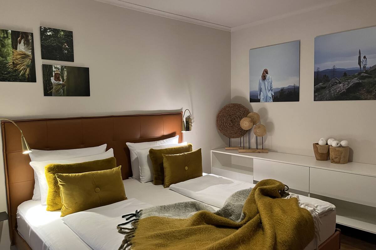 A modern hotel room with a large bed, a bedside table, and a wall-mounted shelf with decorative items.