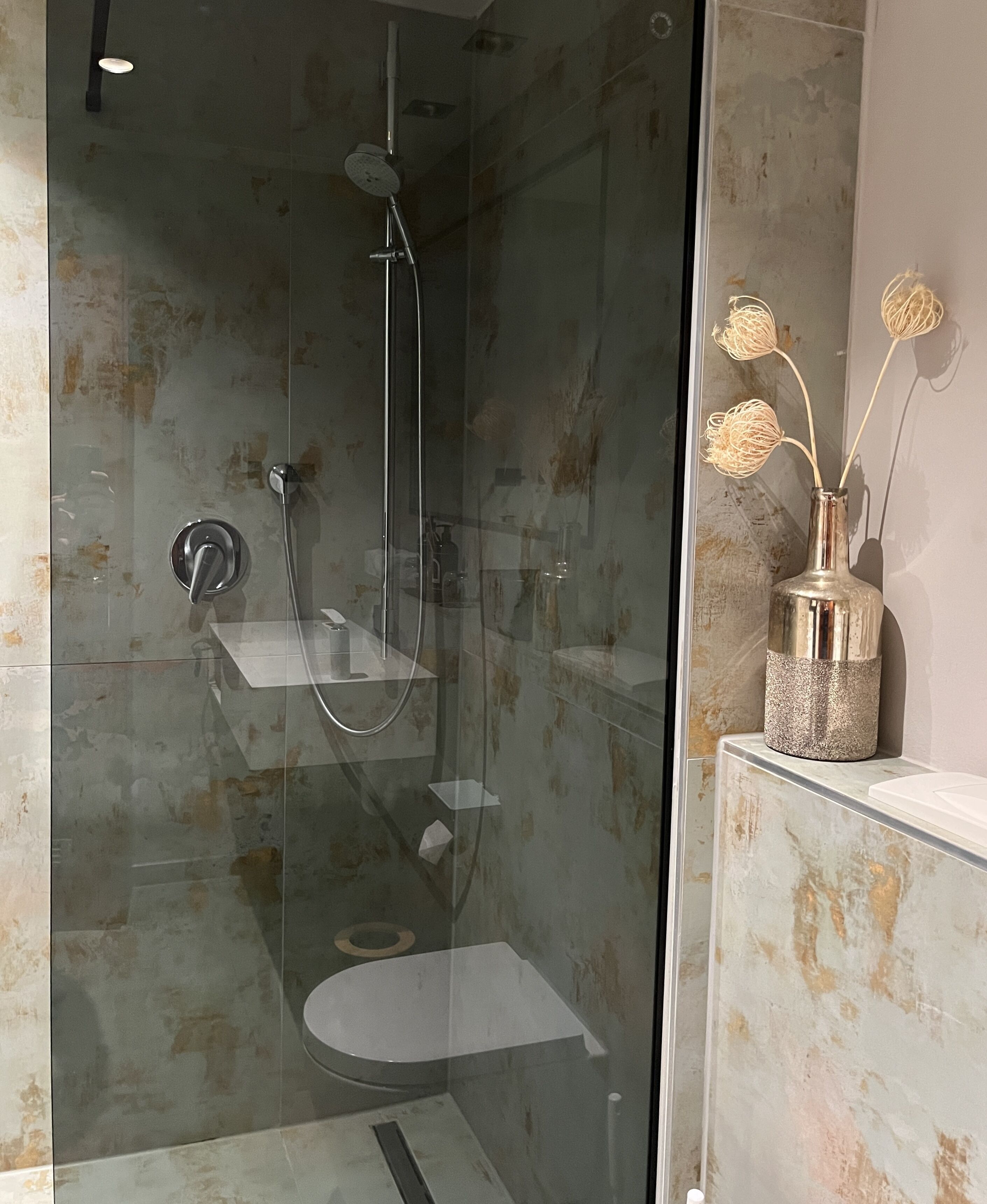 Un baño moderno con ducha envuelta en vidrio, un inodoro y un tocador con un jarrón decorativo.