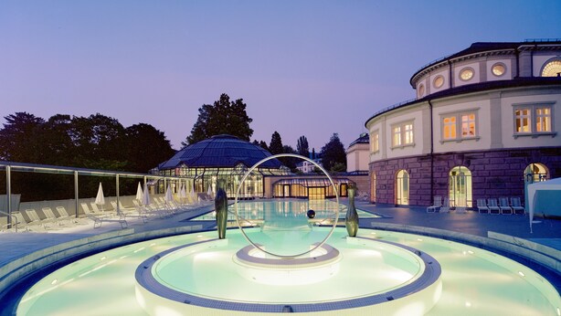 A pool with a circular design, lounge chairs, and a building with classical architecture in the background. - Hotel Schlossberg (Badenweiler)