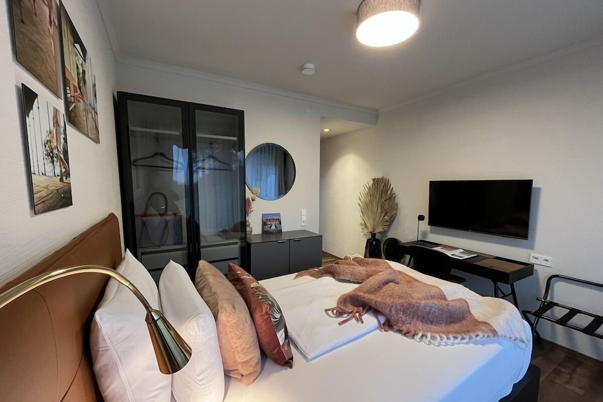 A modern bedroom with a bed, bedside lamp, and a flat-screen TV.