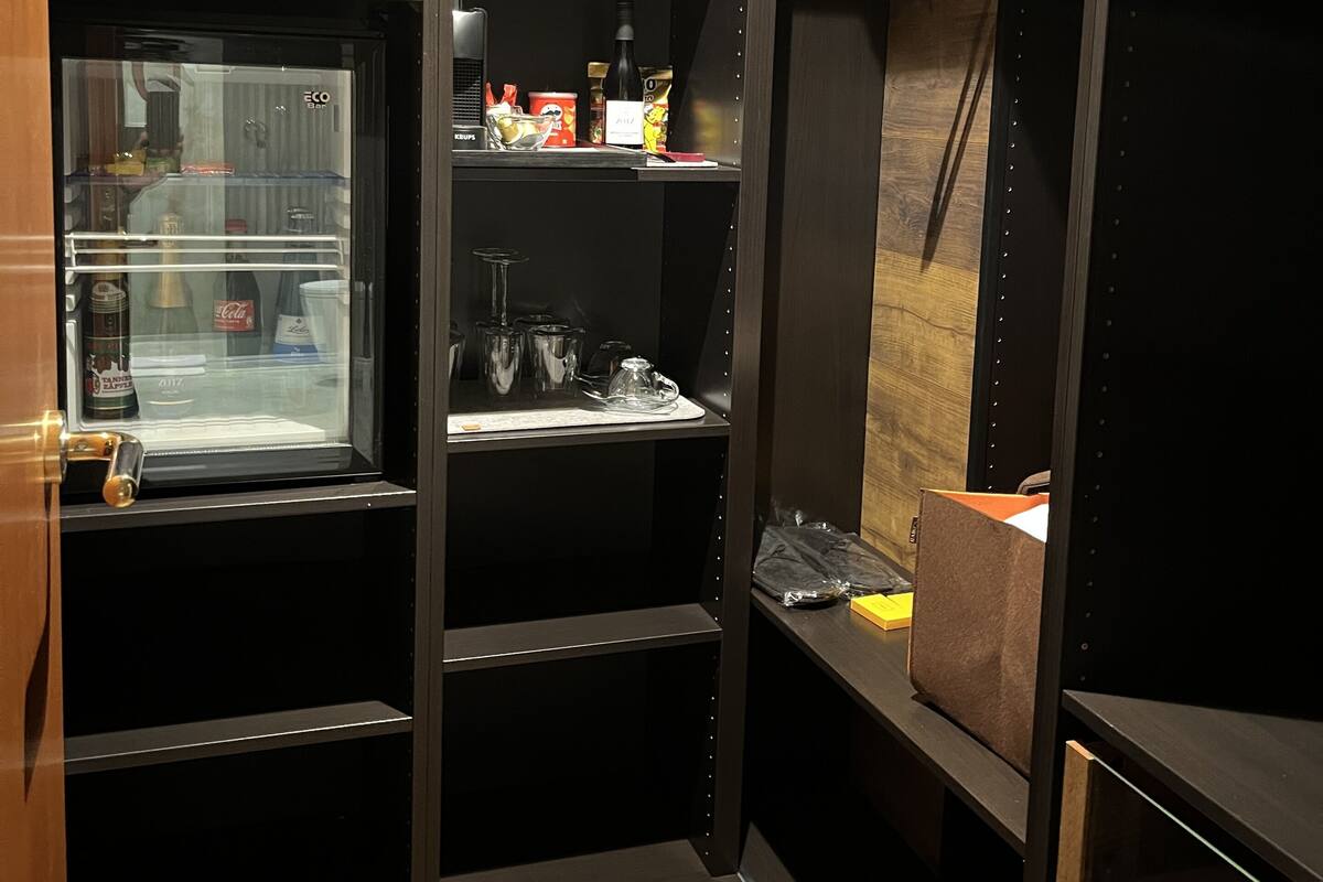 A walk-in closet with shelves, a hanging rod, and a small refrigerator.