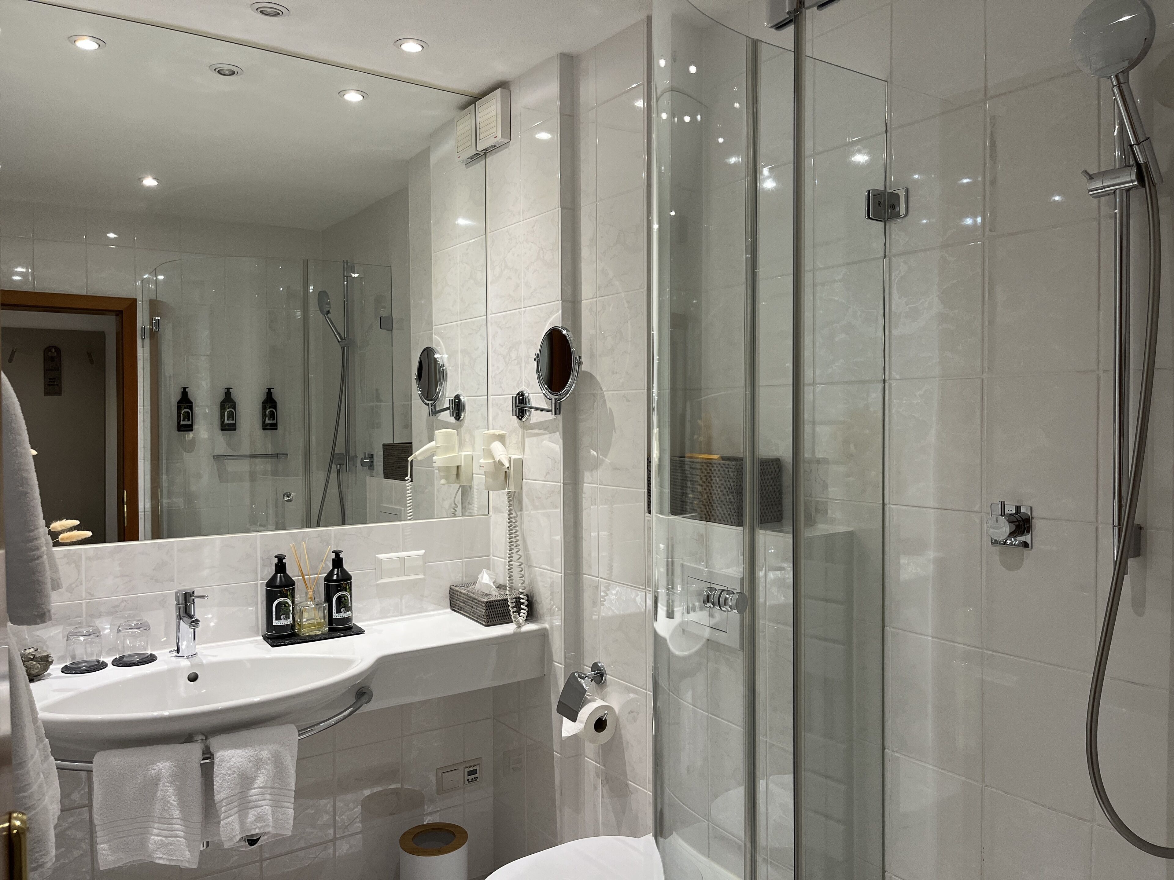 Een moderne badkamer met een douchecabine van glas, een witte wastafel met spiegel en toiletartikelen op het aanrecht.