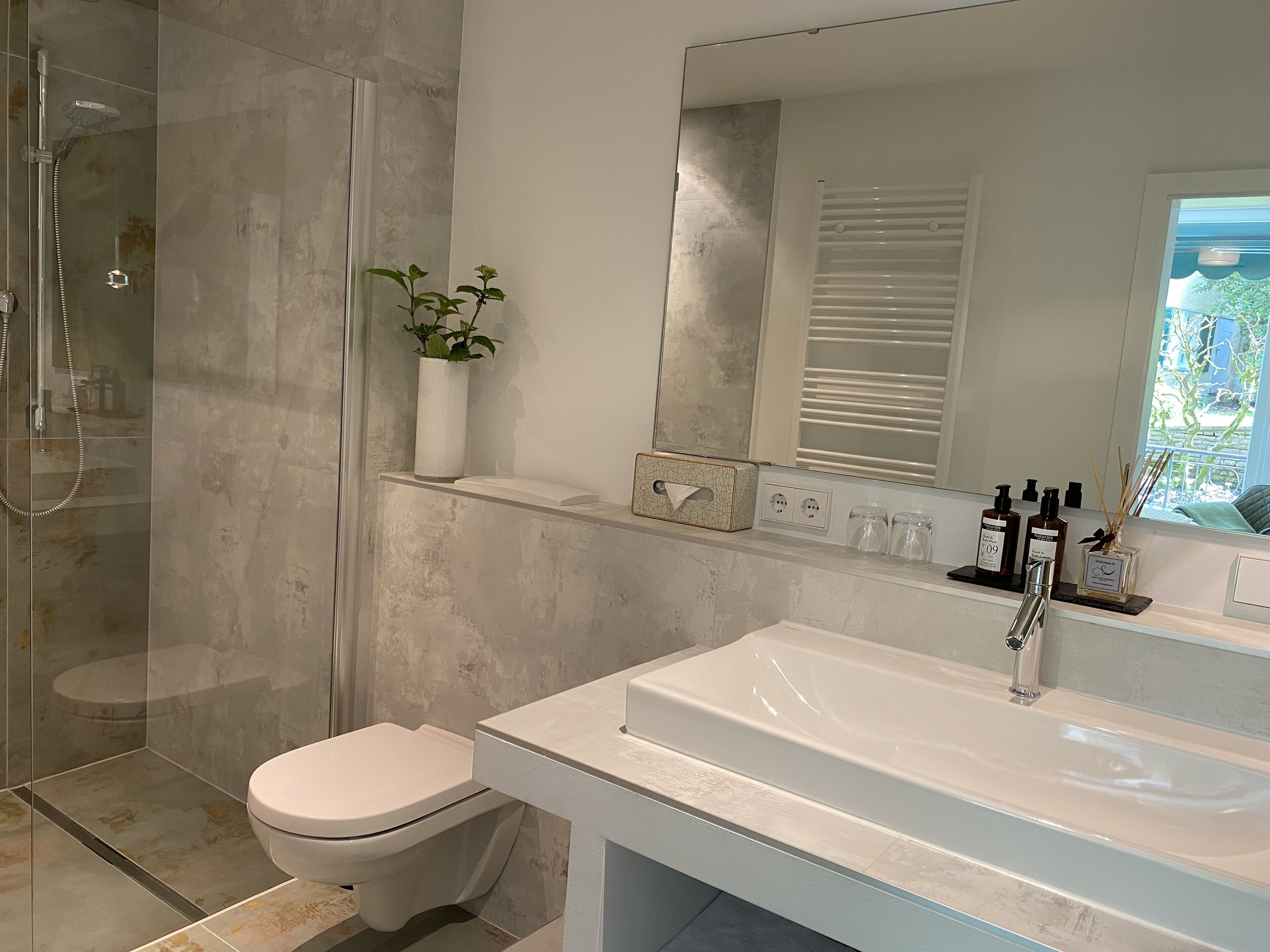 Un baño moderno con cabina de ducha de vidrio, un inodoro blanco, un espejo grande y un lavabo blanco con grifo.