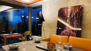 A modern dining area with a table set for two, a sofa, and a large framed picture on the wall. - Hotel Schlossberg (Badenweiler)