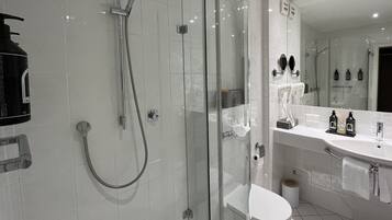 Un baño moderno con ducha envuelta en cristal, inodoro blanco y un espejo grande sobre el lavabo.