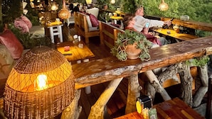 Ein Außenbereich mit Holztischen und -stühlen, umgeben von Grünpflanzen und hängenden Pflanzen.