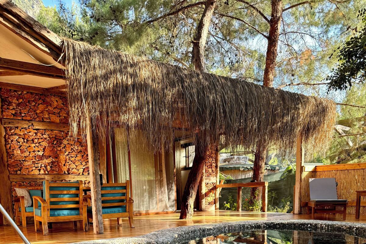 A clear pool with a stone border, wooden deck, and rustic furniture.