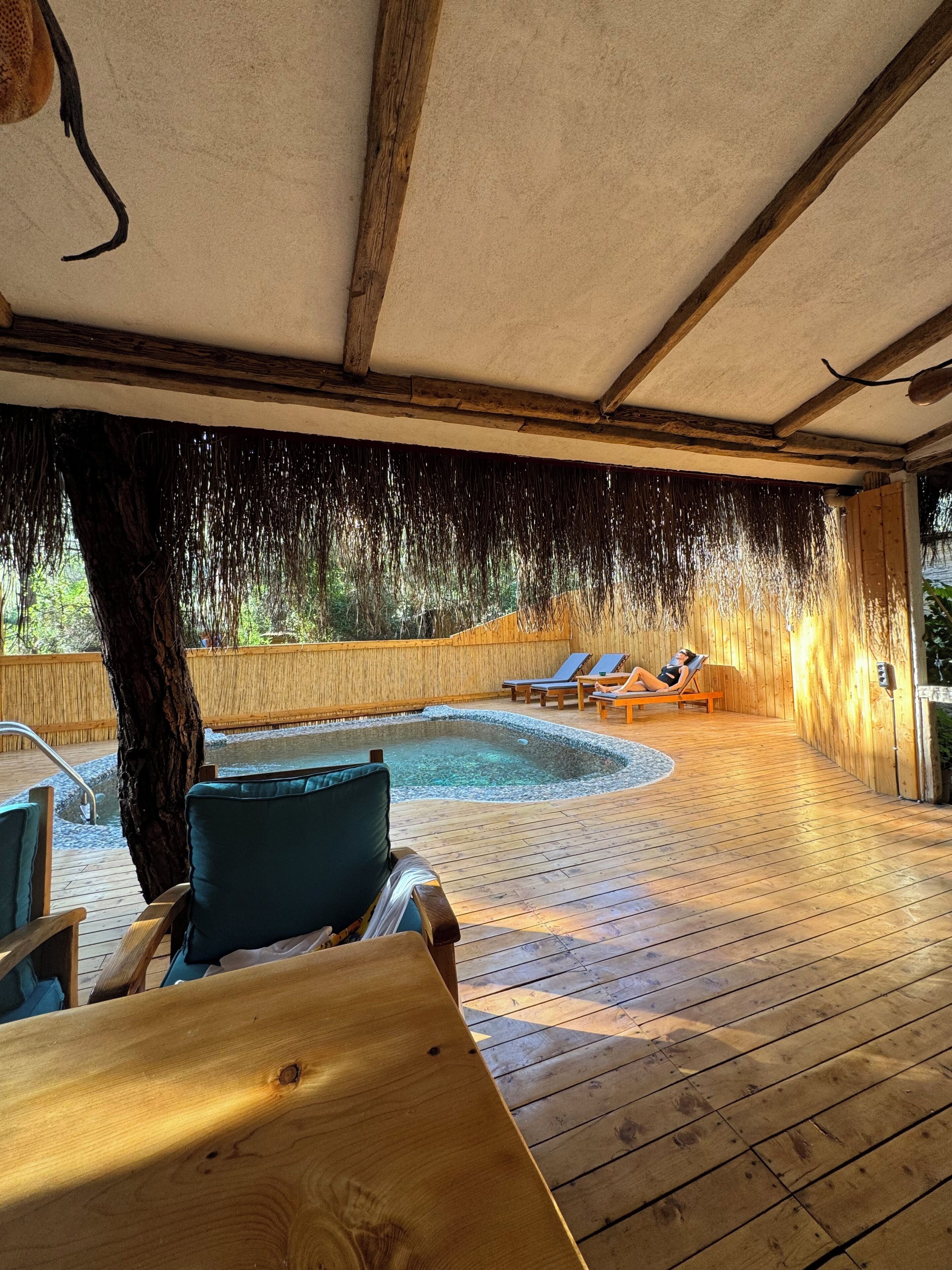 A wooden deck with a pool, lounge chairs, and a covered area.