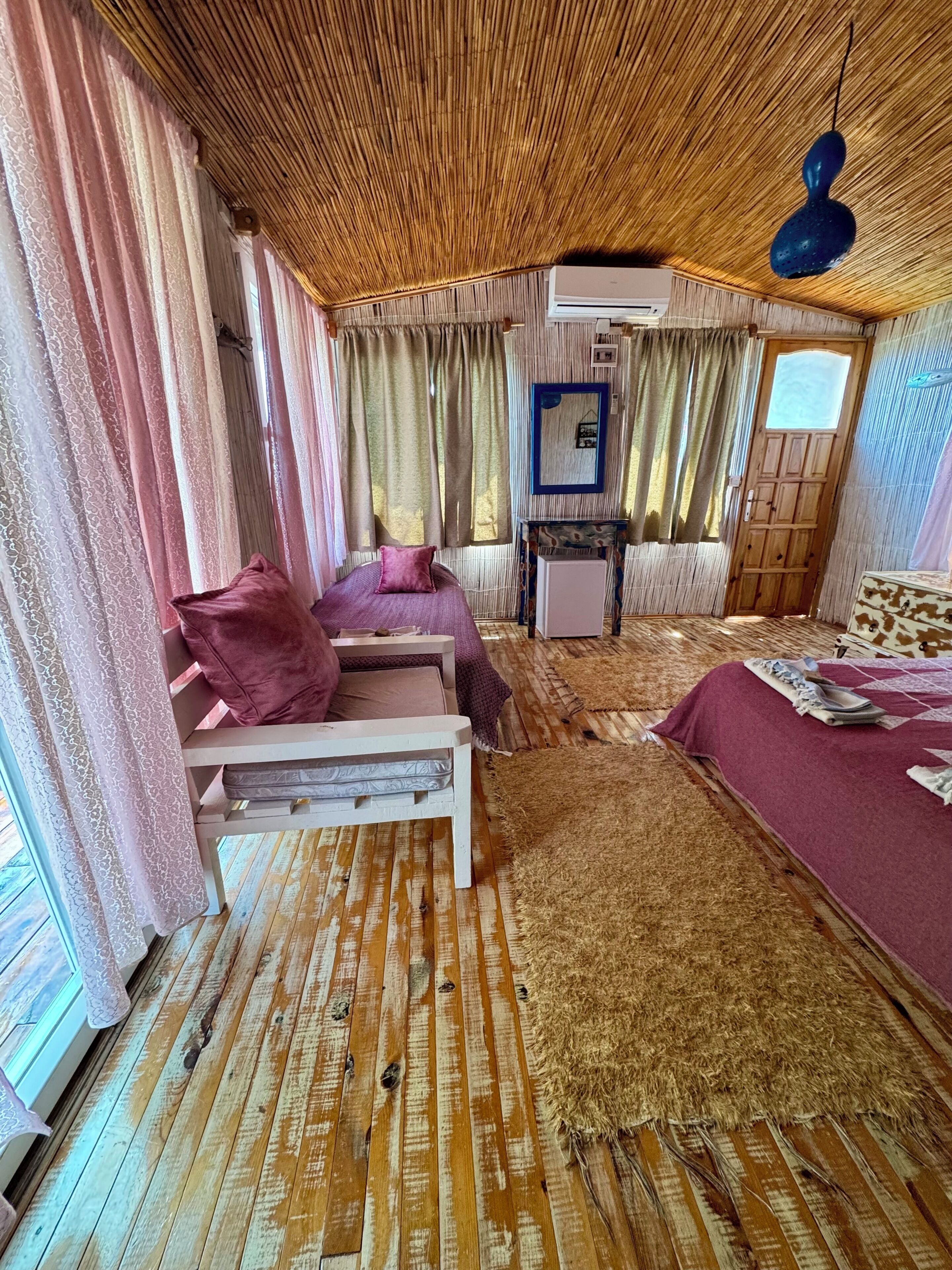 Een kamer met een bed, een klein tafeltje, een spiegel en een raam met gordijnen.