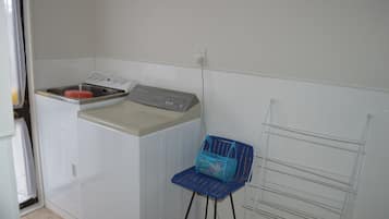 Ein Waschbereich mit Waschmaschine, Wäscheständer und blauem Stuhl.