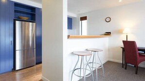 Eine moderne Küche mit einem Edelstahl-Kühlschrank, blauen Schränken und einer Holz Arbeitsplatte. Zwei Hocker und ein roter Stuhl befinden sich in der Nähe eines Tisches mit einer Lampe.