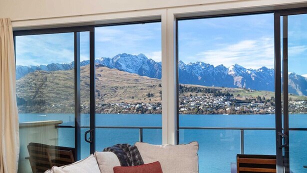 Ein Zimmer mit einer großen Schiebeglasdoor, die zu einem herrlichen Blick auf Berge und einen See führt.