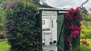 Une petite salle de bain extérieure privée, dotée d’un lavabo et d’un miroir blancs, et entourée d’une végétation luxuriante et de plantes en fleurs.