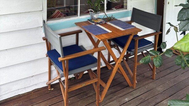 Une terrasse en bois avec une table et des chaises, une pancarte indiquant « Quail Cottage », et une fenêtre donnant sur l’extérieur.