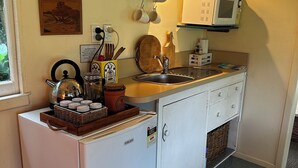 Une cuisine compacte équipée d’un réfrigérateur, d’un four à micro-ondes et d’un petit évier. On y trouve divers ustensiles de cuisine et une machine à café sur le plan de travail.