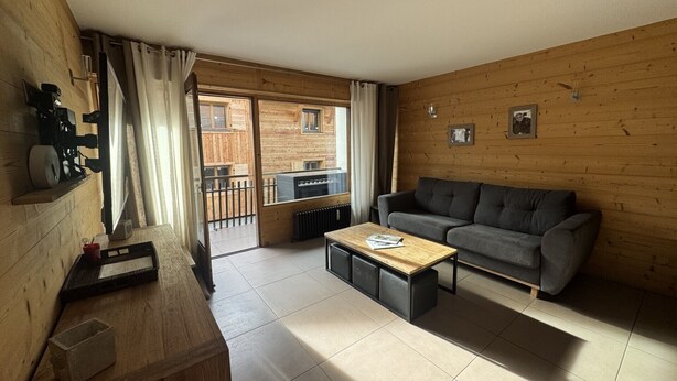 A cozy living room with a sofa, a coffee table, and a wooden floor. There is a sliding glass door leading to an outdoor area. - Beautifully appointed mountain studio, close to the village of Megève, sleeps 4. (Megève)