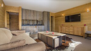 A modern living room with a sofa, a coffee table, and a TV mounted on the wall. - Beautifully appointed mountain studio, close to the village of Megève, sleeps 4. (Megève)