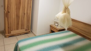 A room with a wooden wardrobe, a bedside table with a lamp, and a bed with a striped bedspread. - Renting a furnished tourist apartment with sea view (ANSES-D ARLET)