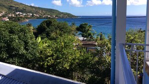 A coastal view with a balcony overlooking the sea, lush greenery, and distant houses. - Renting a furnished tourist apartment with sea view (ANSES-D ARLET)