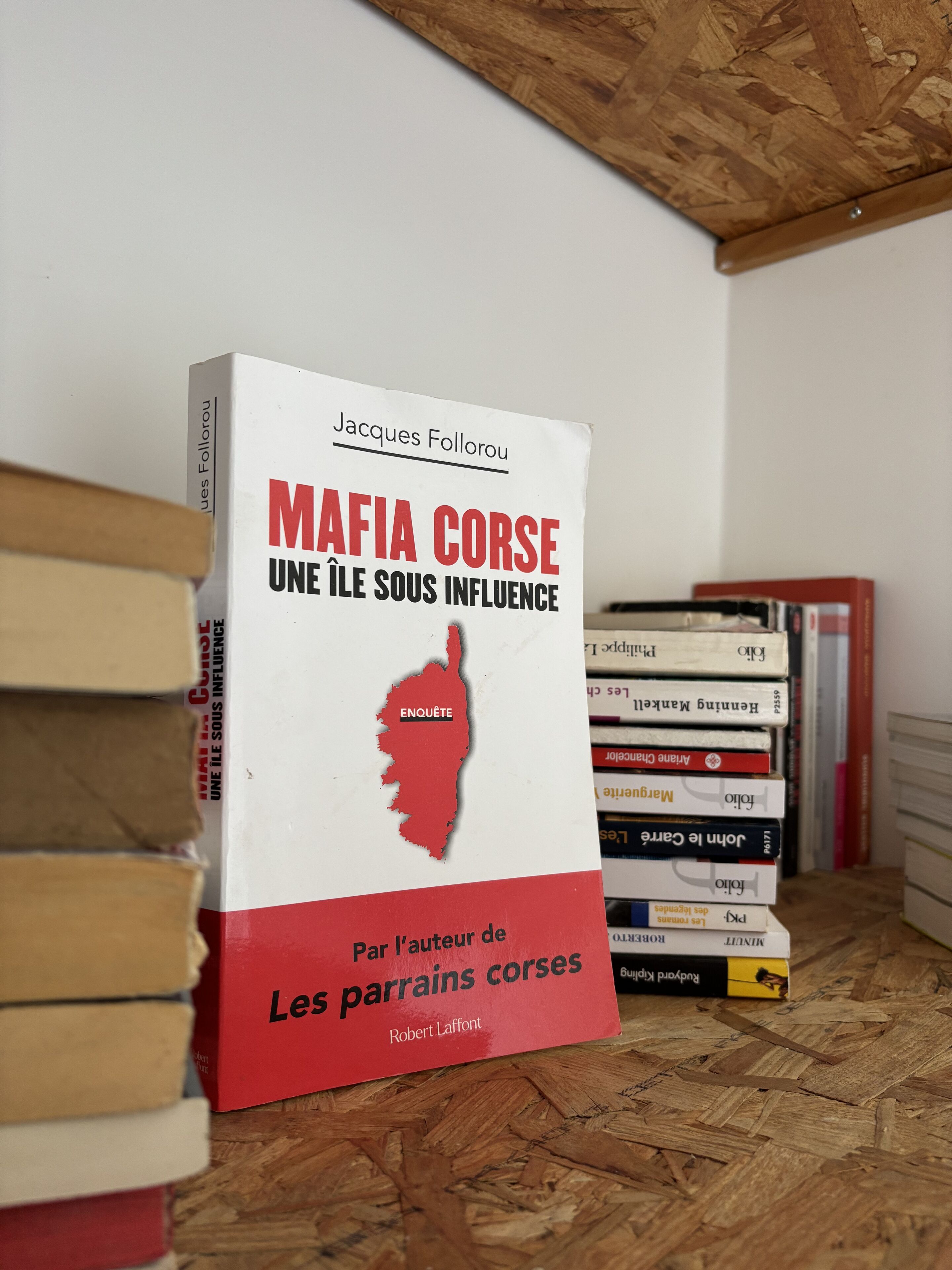A book titled 'MAFIA CORSE' by Jacques Follorou, placed on a wooden surface with other books around it.