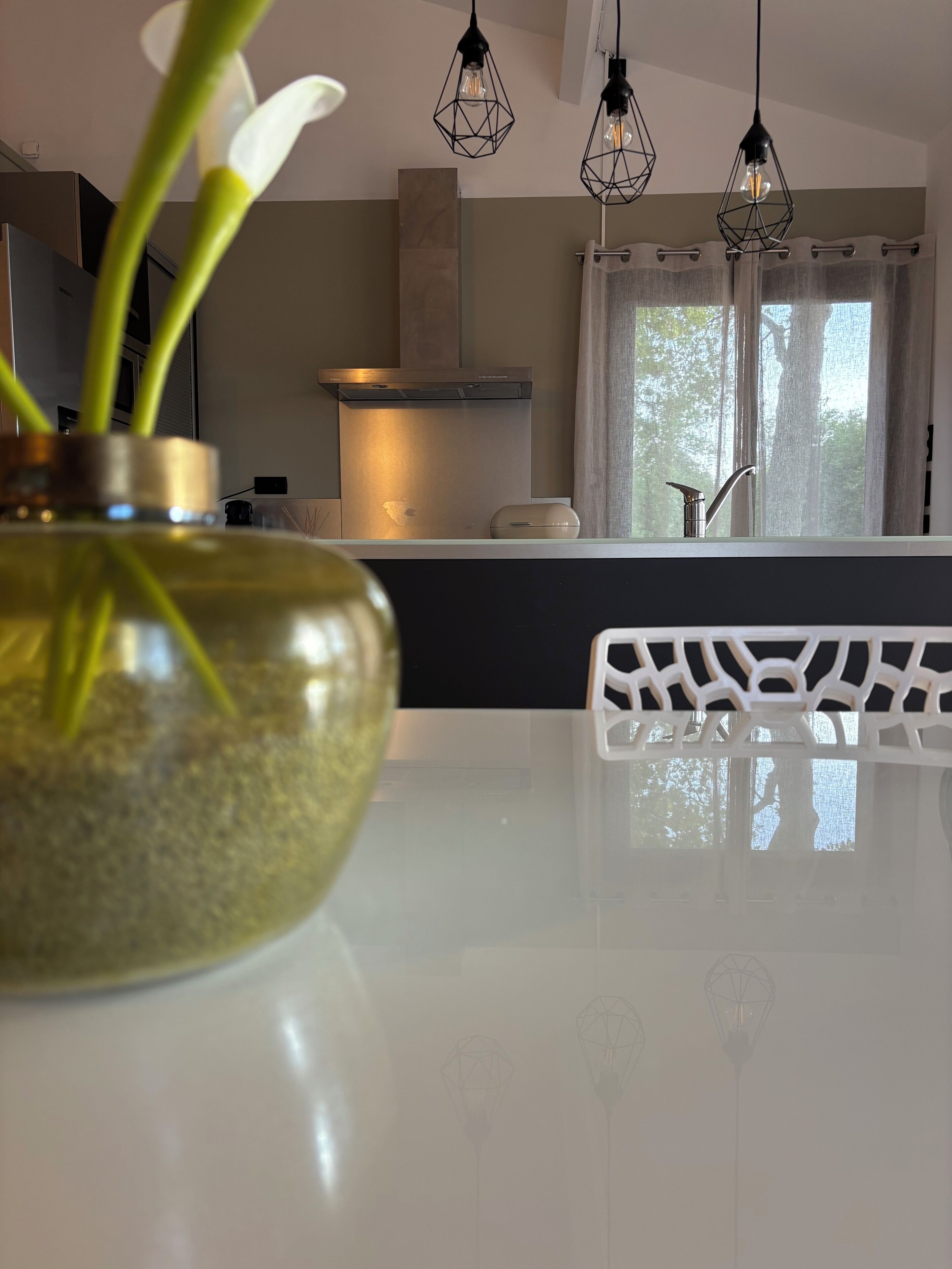 Une cuisine moderne avec un plan de travail blanc, un vase contenant des plantes vertes et des luminaires suspendus.